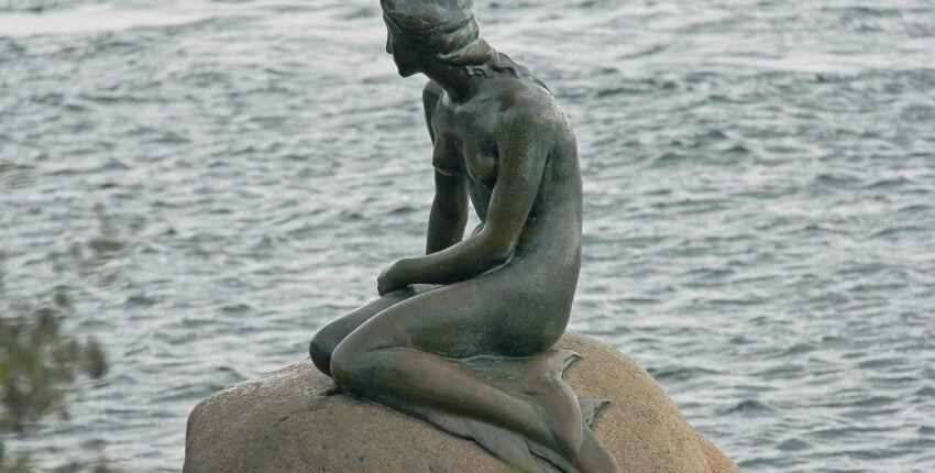 Une statue de sirène assise sur un rocher.