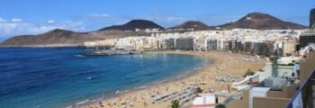 Las Palmas Gran Canaria plage bondée, eau bleue, montagnes.