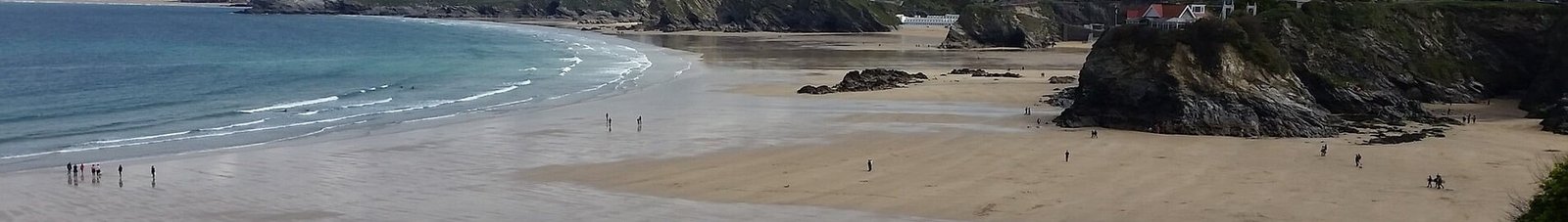 Plage Newquay, Cornouailles avec falaises rocheuses et bâtiments.