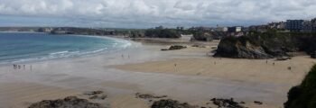 Plage Newquay, Cornouailles avec falaises rocheuses et bâtiments.