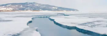 Glace craquelée sur un lac gelé avec des montagnes enneigées sous un ciel nuageux au loin, rappelant les paysages pittoresques près d'Irkutsk. - GCD Logistique Aviation