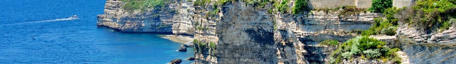 **Texte alternatif :** Corse : Ville colorée, mer bleue, et bateau en-dessous.